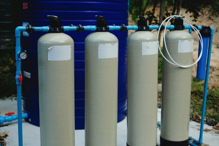 pexels-photo-12726229-12726229 Four beige tanks in an outdoor water treatment setup with blue piping.