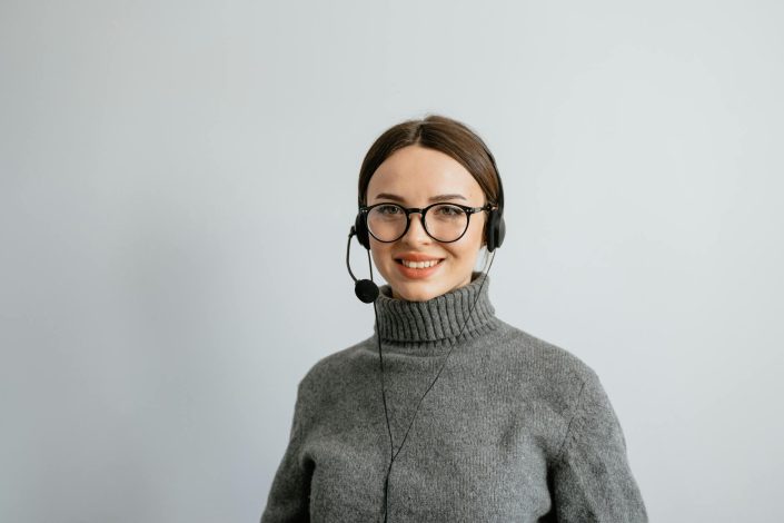 pexels-photo-7709263-7709263 Smiling female call center agent wearing headphones and a gray sweater, ready to assist.